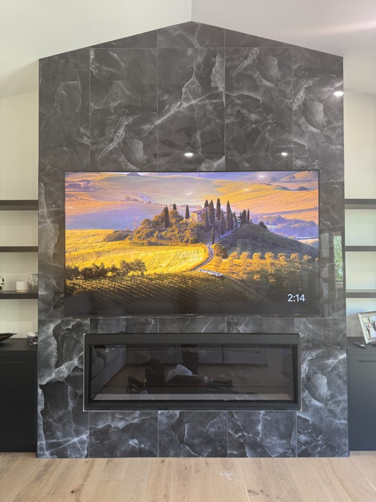 TV mounted above a fireplace on a dark marble feature wall by Hamilton Tech Source